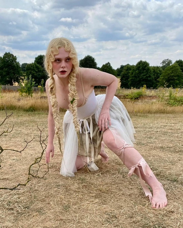 Elle Fanning poses sexily in a white dress that barely holds back her boobs